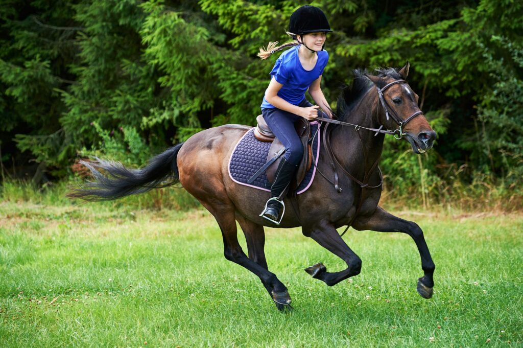 Side view of girl wearing riding hat galloping on horseback